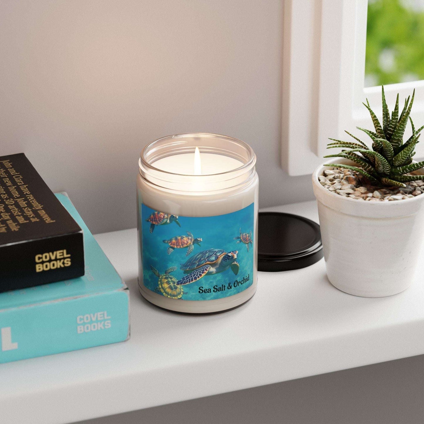 Soy candle labeled "Sea Salt & Orchid" on a shelf with books and a potted plant.