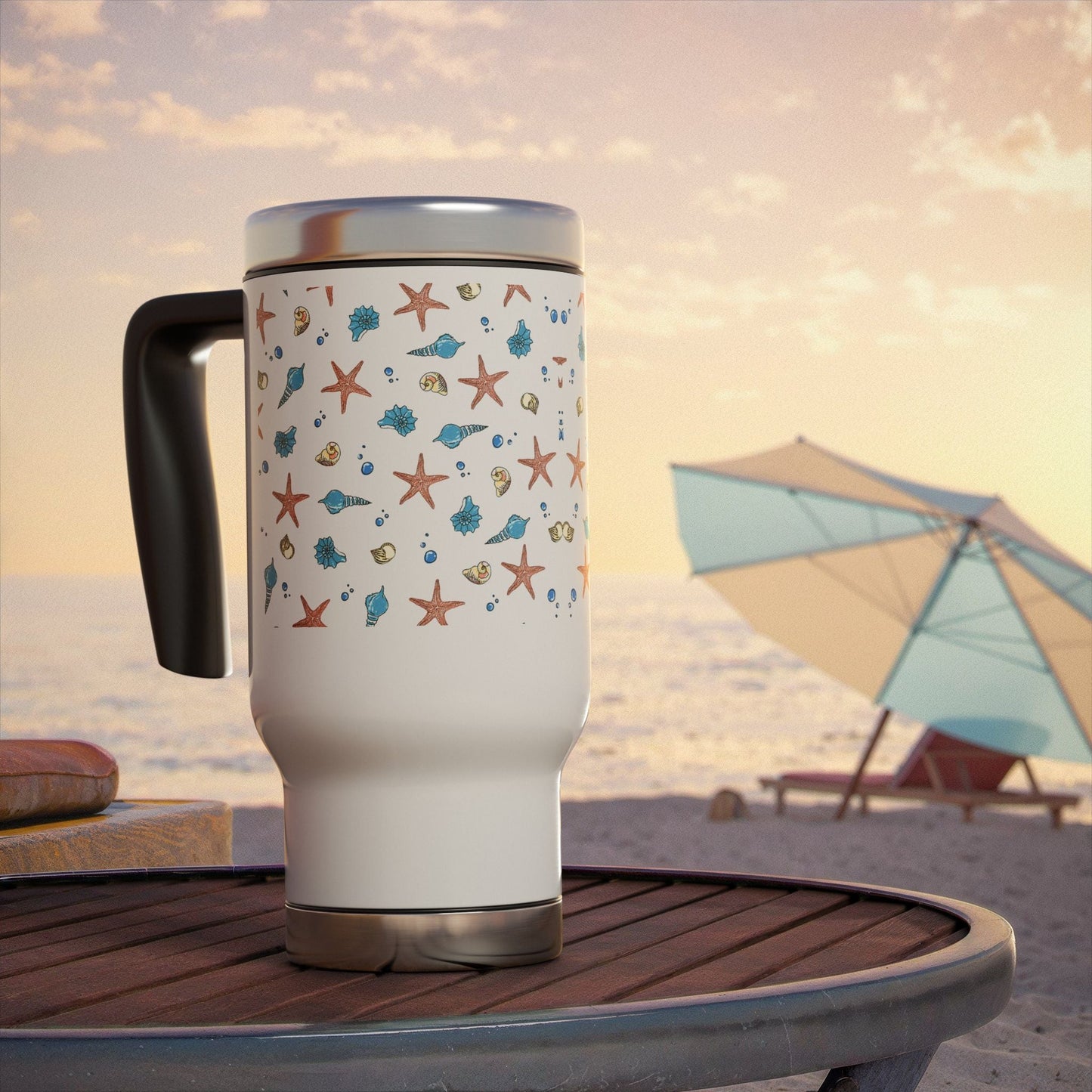 Stainless steel coffee mug with beach theme and handle on a beach table.
