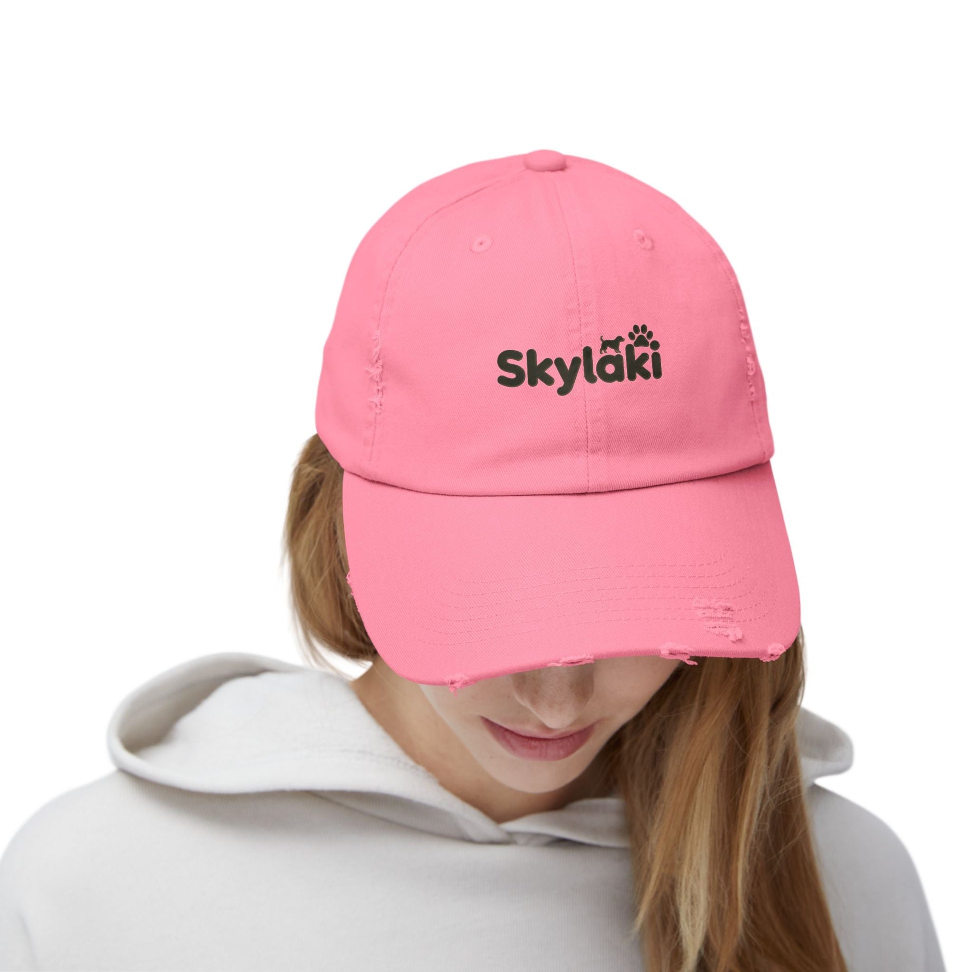Unisex distressed cap with Skylaki logo, pink cotton twill, curved visor, eyelets, and adjustable strap.