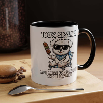 Ceramic coffee mug with a white exterior, black interior and handle, showing a sunglasses-wearing dog and Will Work for Souvlaki and Belly Rubs text